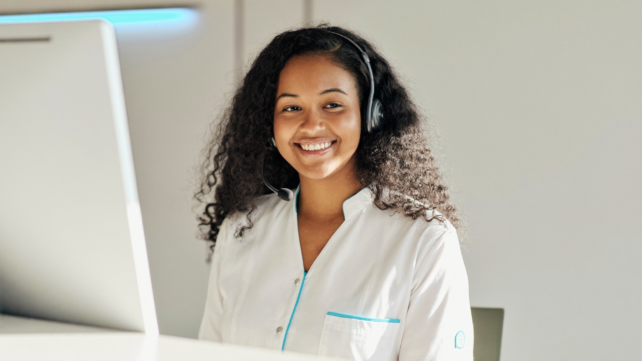 Recepcionista sorrindo ao atender em uma recepção de clínica moderna e clara